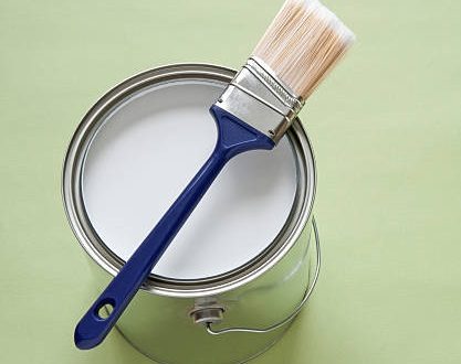 Paintbrush and a newly opened can of white paint on green background.